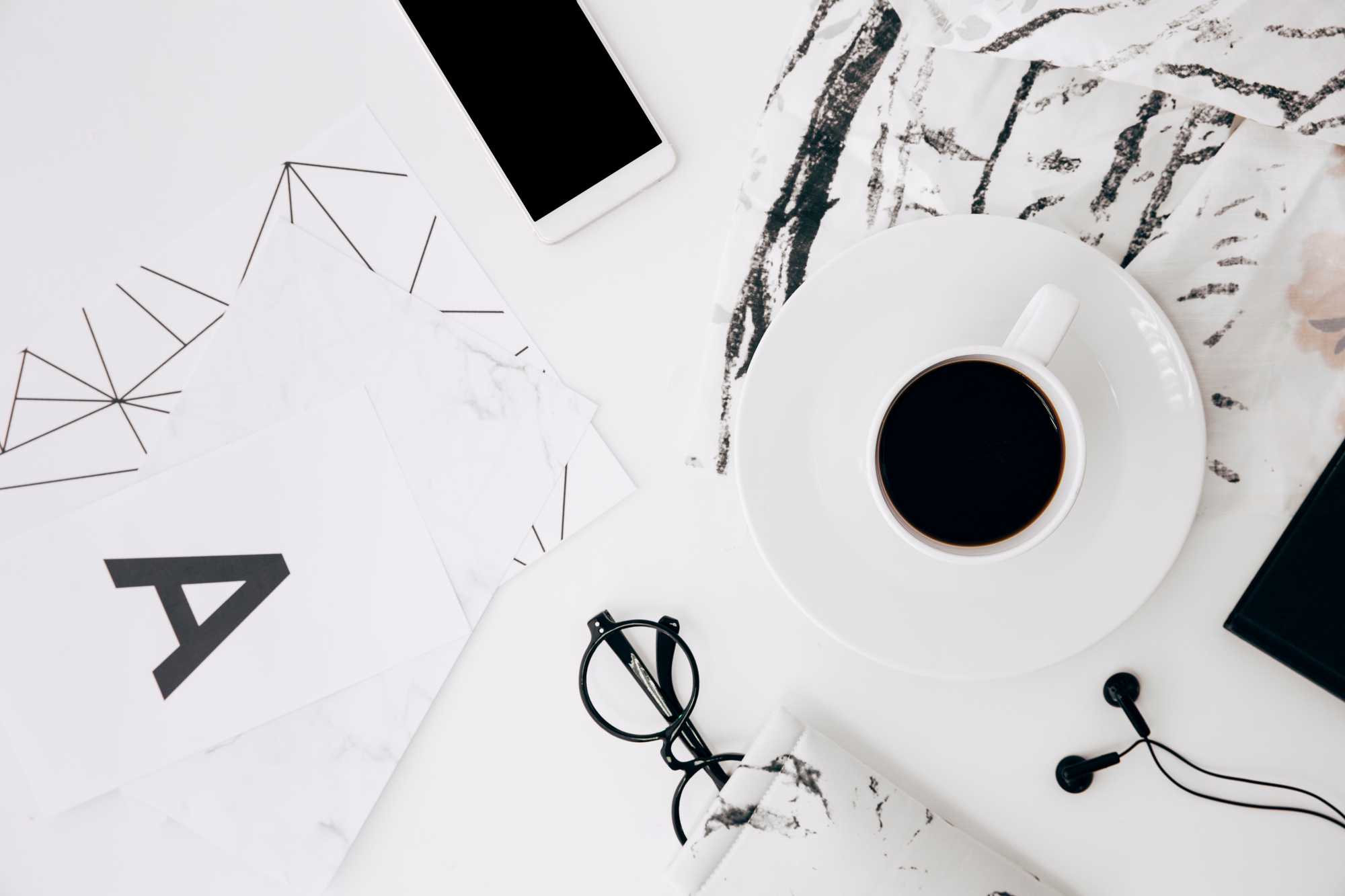 letter-eyeglasses-smartphone-earphone-coffee-cup-white-desk